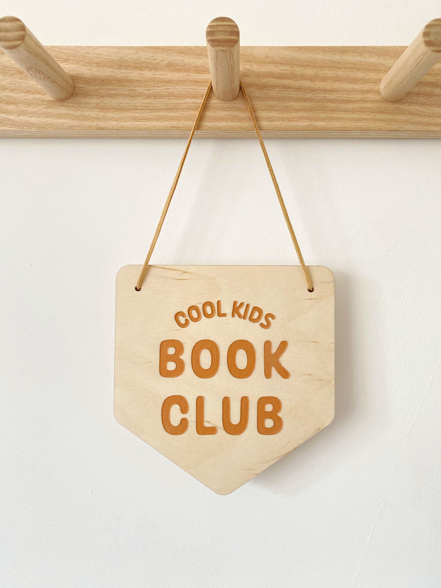 Wooden sign with 'Cool Kids Book Club' text hanging on a wooden rack.