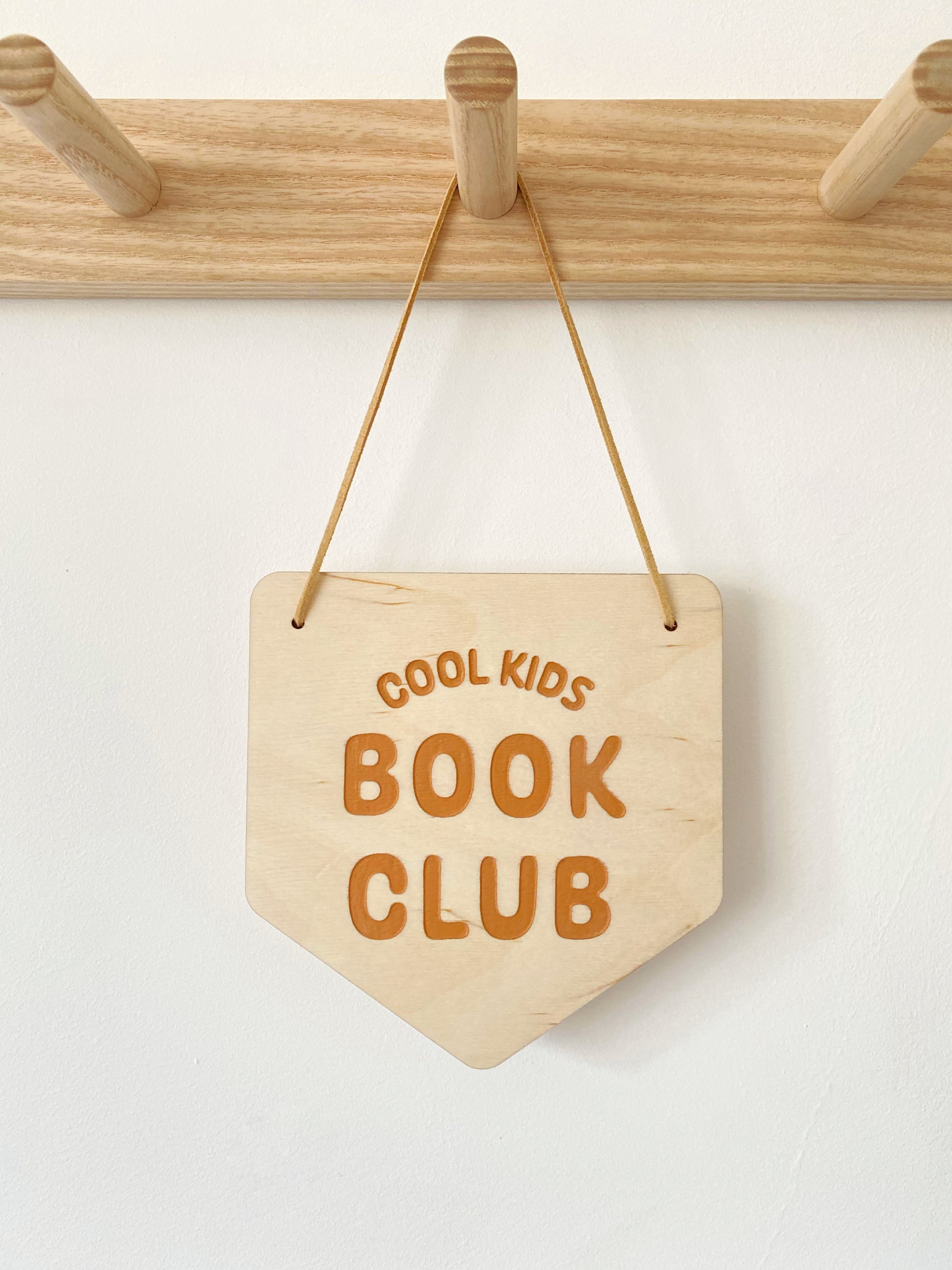 Wooden sign with 'Cool Kids Book Club' text hanging on a wooden rack.