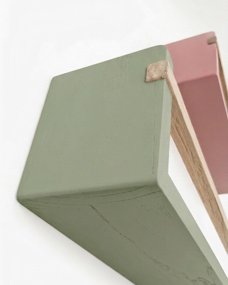 Close-up of olive and dusky pink wooden bookshelf corner on a white background